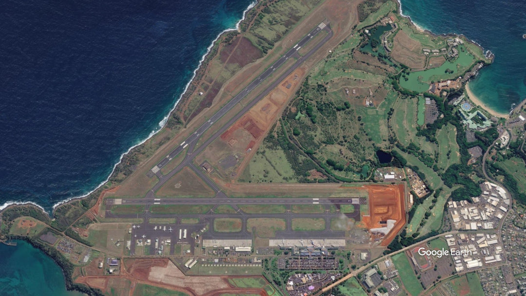 Aerial view of Lihue Airport in Kauaʻi, Hawaii, showing its two runways, terminal area, surrounding coastline, and nearby green landscape.